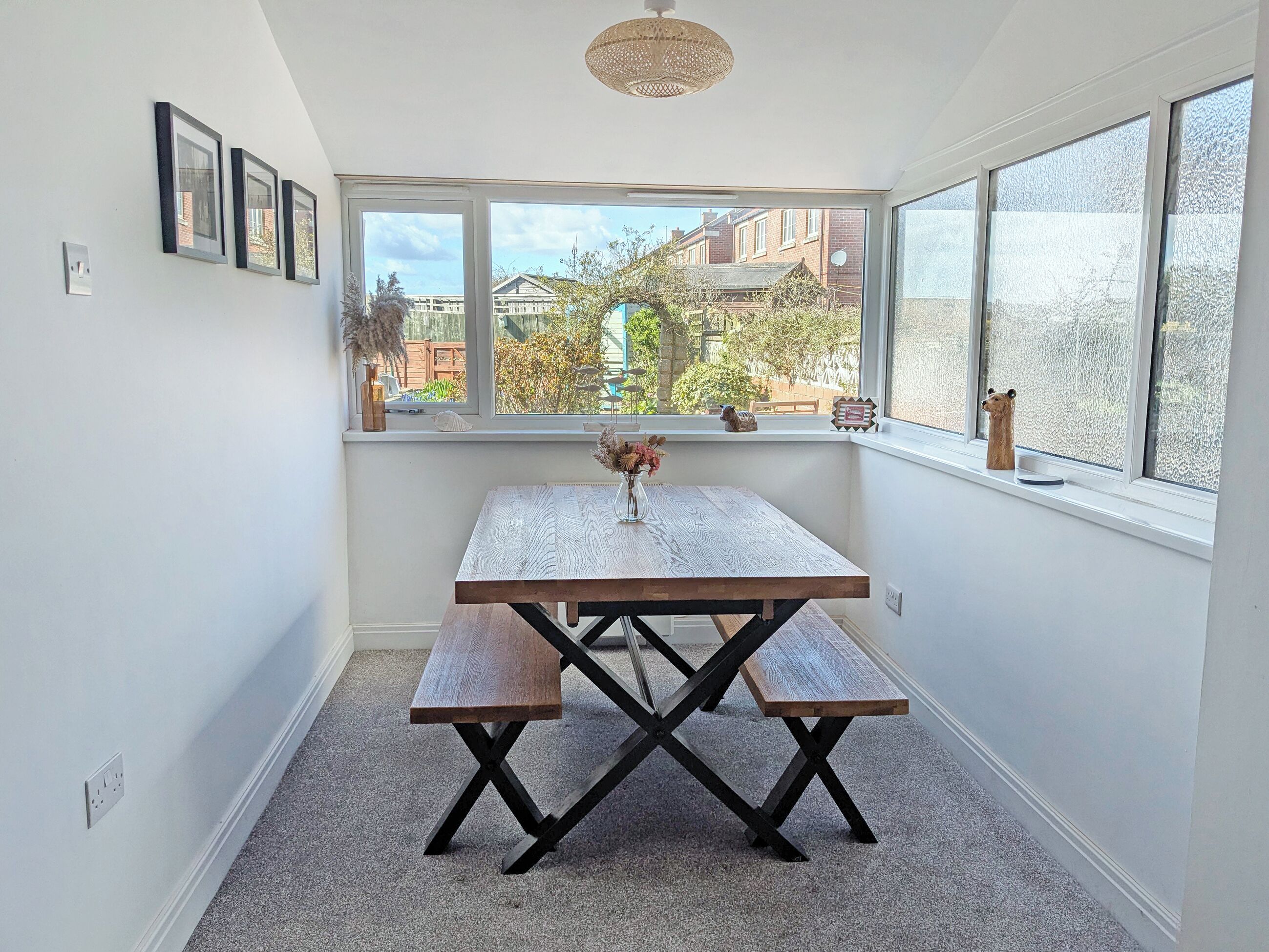 A corner room with a wooden table and bench, a window with frosted glass, and a view of buildings outside.