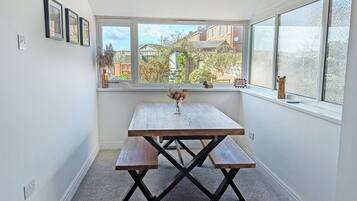 A corner room with a wooden table and bench, a window with frosted glass, and a view of buildings outside.