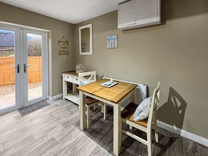 A room with a wooden table and chairs, a white radiator, a door leading outside, and a small white cabinet. - 3 bedroom accommodation in Chapel St. Leonards (Chapel St. Leonards)