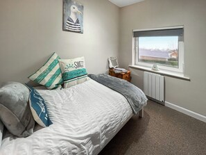 Een slaapkamer met een bed, kussens, een nachtkastje, een raam en een radiator.