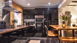 Een moderne keuken met zwarte kasten, roestvrijstalen apparatuur, een houten bar en een accentmuur van steen.