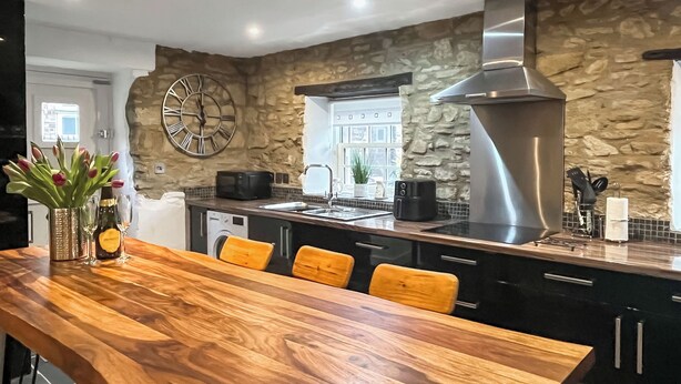Een moderne keuken met een stenen muur, een grote klok, een houten eettafel en een inbouwoven.