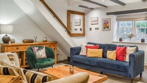 Een kamer in loftstijl met zichtbare balken, een blauwe bank, een houten salontafel en een groene fauteuil.