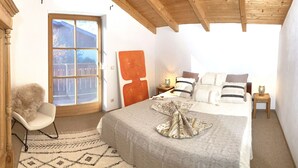 Une chambre à coucher avec un grand lit, une chaise, une armoire en bois, une fenêtre et une table de chevet avec une lampe.