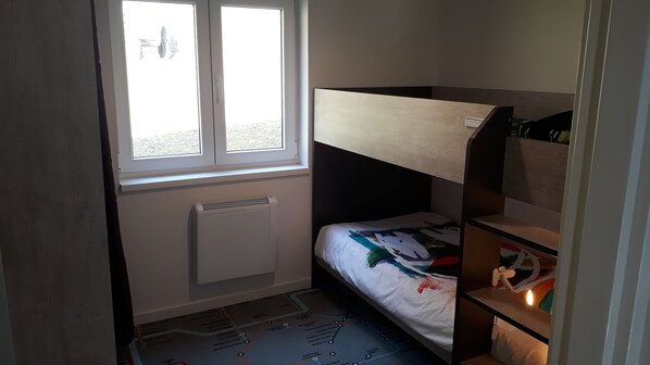 A small, well-lit room with a bunk bed, a radiator, a window, and a map on the floor.