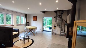 Een moderne woonkamer met een eethoek, grote ramen en een trap.