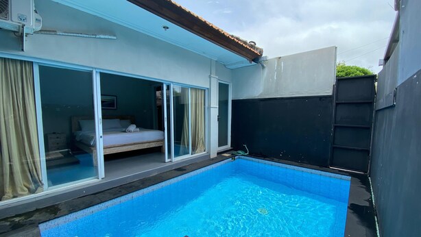 A swimming pool with a glass enclosure, a bed with a white mattress, and a sliding glass door. - Villa Kulat (Pecatu)