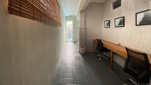 A hallway with a wooden slatted wall, a tiled floor, a desk with chairs, and framed pictures on the wall. - Villa Kulat (Pecatu)