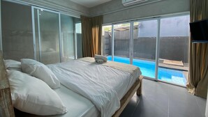 A bedroom with a large bed, a sliding glass door leading to a pool area, and an air conditioning unit on the wall. - Villa Kulat (Pecatu)