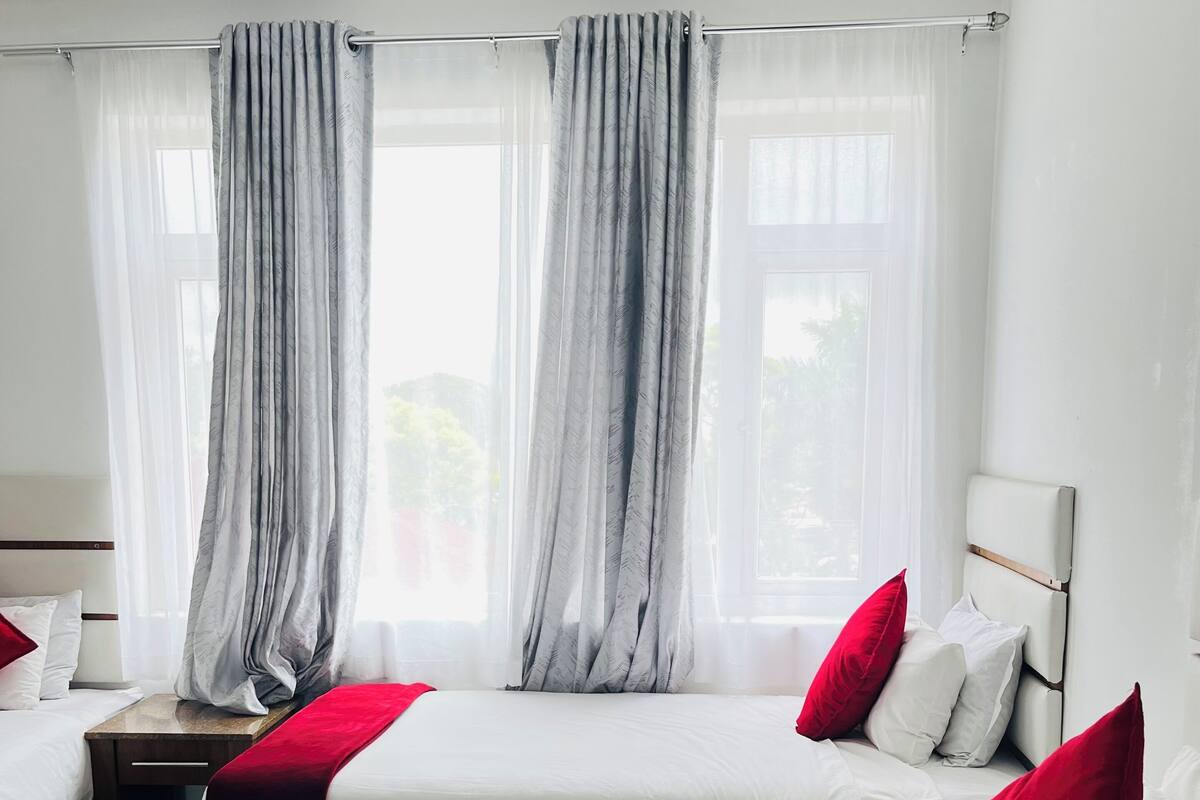 Habitación de hotel con dos camas, ropa de cama blanca, almohadas rojas y cortinas de gasa.