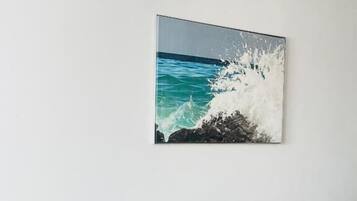 Un canapé à rayures vertes, agrémenté de coussins jaunes et verts, est placé devant un mur blanc. Au-dessus, on peut voir un tableau encadré représentant une vague se brisant sur des rochers.