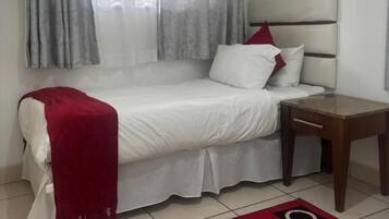 A single bed with a red throw blanket, a bedside table, and a patterned rug.