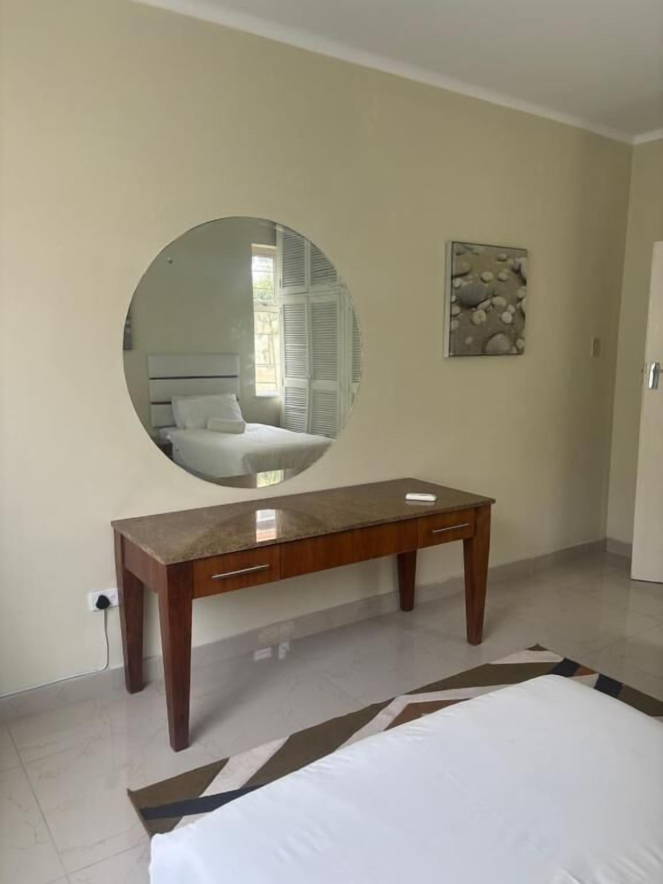 A bedroom with a bed, a wooden nightstand, a round mirror, and a small table.
