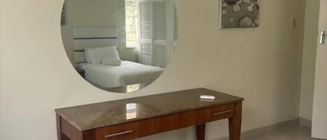 A bedroom with a bed, a wooden nightstand, a round mirror, and a small table.