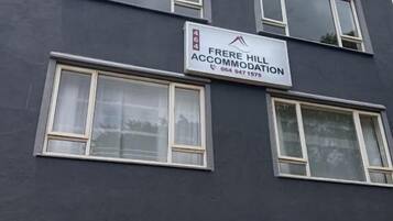 Een meerlaags gebouw met een bord waarop 'Frere Hill Accommodation' staat en een contactnummer.