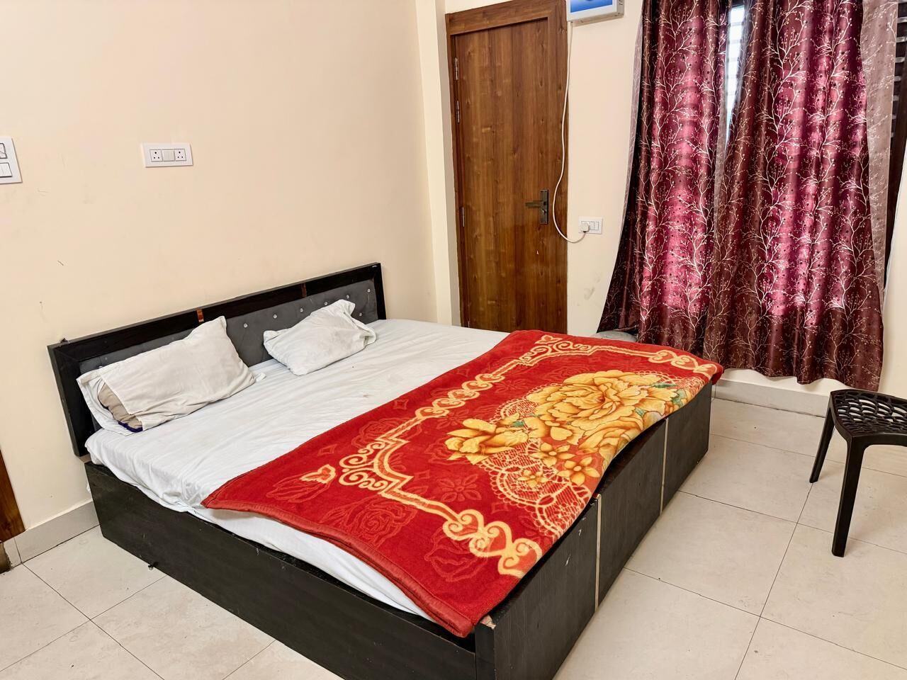 Uma cama com colcha florida vermelha, cabeceira de madeira e almofadas brancas.