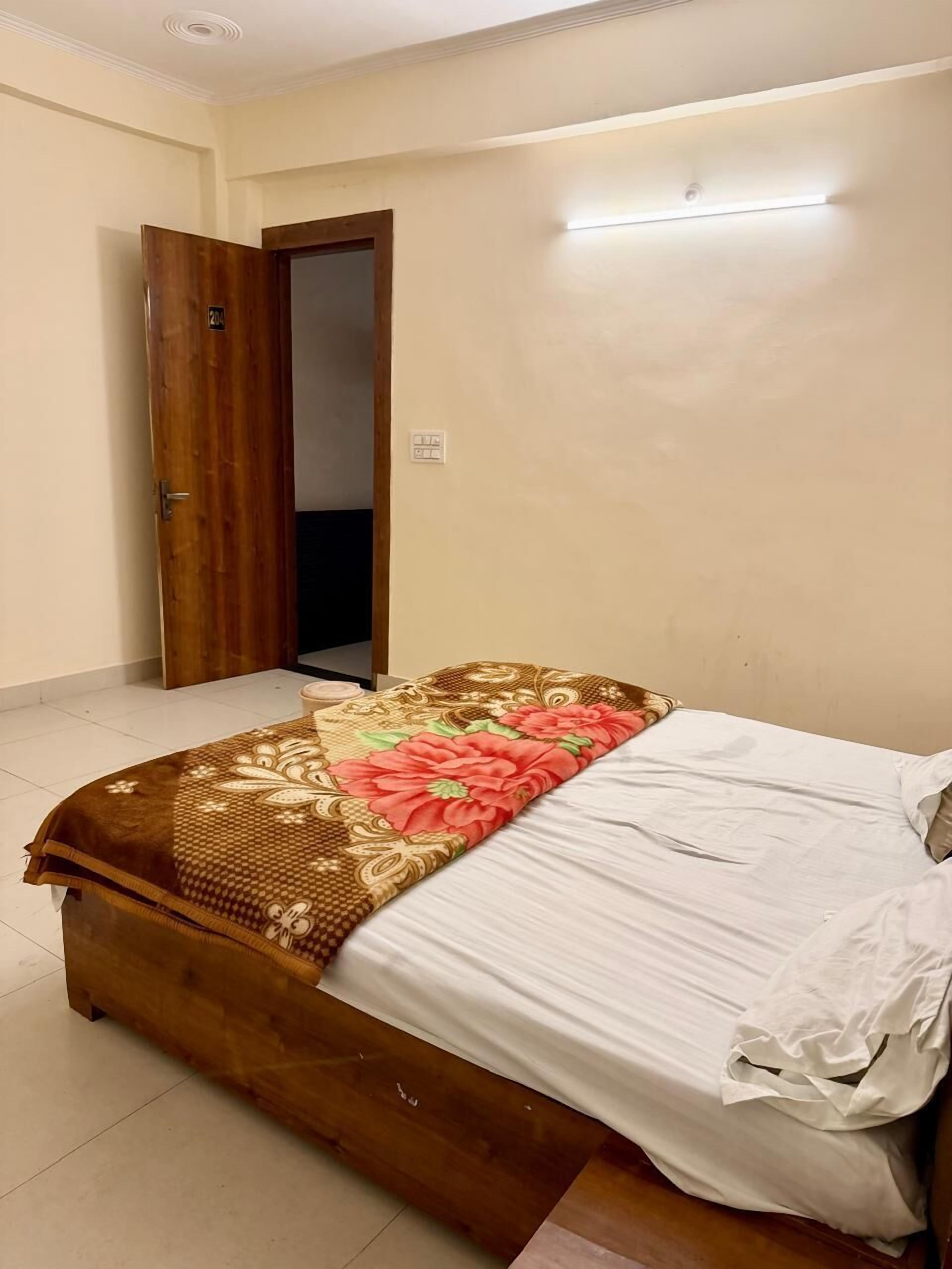 Ein Schlafzimmer mit einem hölzernen Bett, einer blumigen Tagesdecke und einer weißen Wand mit Lichtschalter.