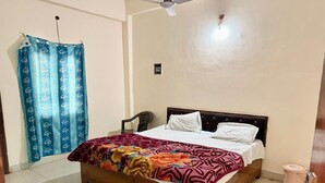 Un dormitorio con cama de madera, cortina azul, ventilador de techo y pared blanca.