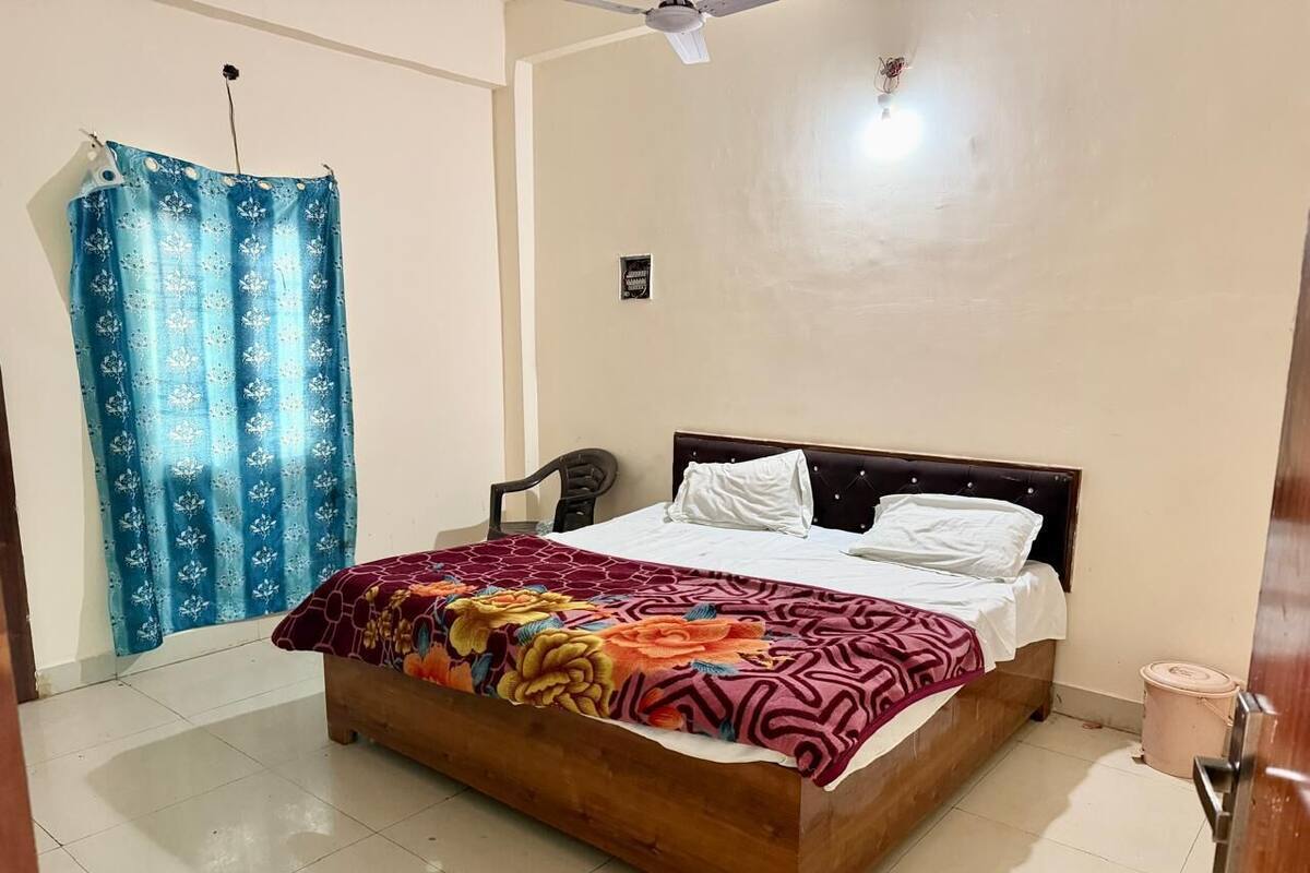 Quarto com cama de madeira, cortina azul, ventilador de teto e parede branca.