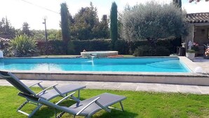 A swimming pool with a fountain, surrounded by grass and trees. There are two lounge chairs in the foreground. - Villa Near Avignon With Separate Suites (Robion)
