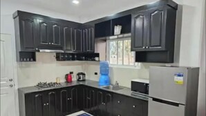A modern kitchen with dark cabinetry, a gas stove, a refrigerator, and a water dispenser. - Beautiful 2-bedroom apartment with AC, beach front and huge parking lot (Opol)
