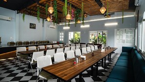 A conference room with a checkered floor, white chairs, a long wooden table, and hanging plants.