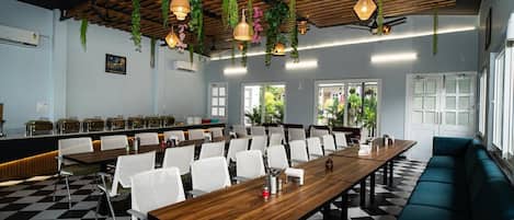 A conference room with a checkered floor, white chairs, a long wooden table, and hanging plants.