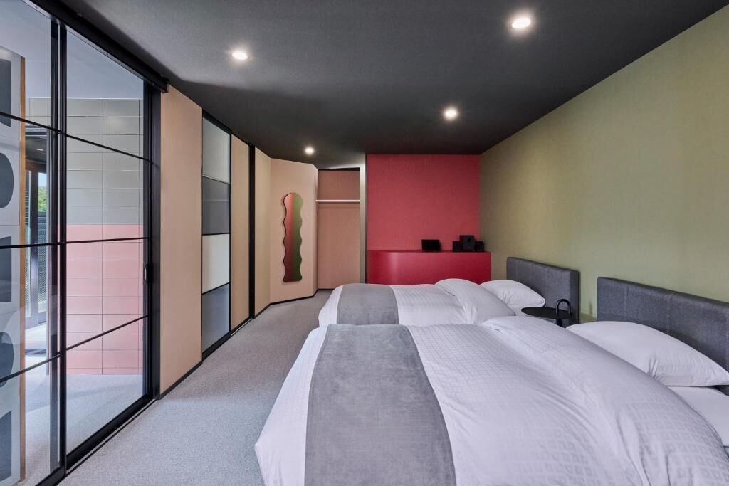Een hotelkamer met twee bedden, een rode accentmuur en een groot raam.