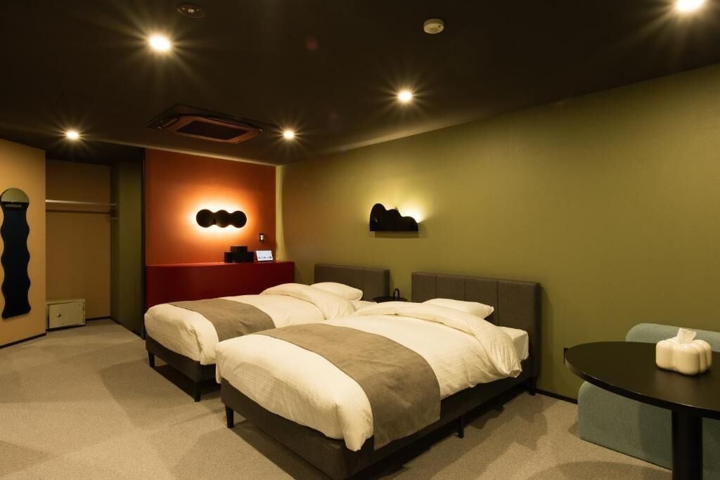 A hotel room with two beds, a small table, and a wall-mounted light fixture.