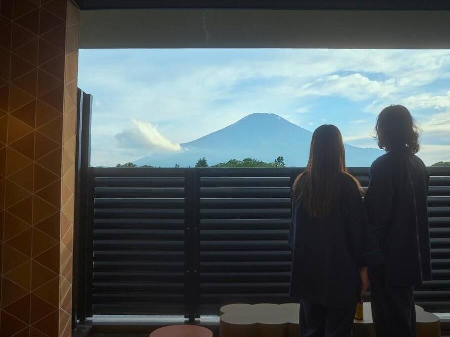 Two people standing by a window with a view of a mountain.