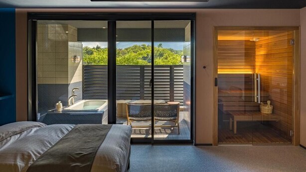 Une chambre moderne avec un grand lit, une porte vitrée donnant sur un balcon équipé d’une baignoire et d’un coin salon.