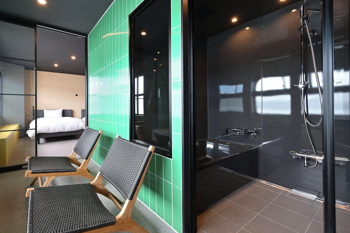 Habitación de hotel con cama, dos sillas, ducha y vistas al exterior.