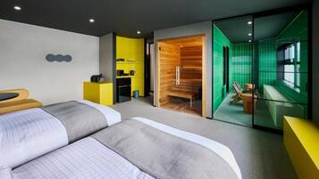 A modern hotel room with a large bed, a small desk, a seating area with a chair and table, and a view of a green-tiled room.