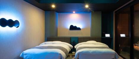 Een hotelkamer met twee bedden, een kleine tafel en een wandlamp.