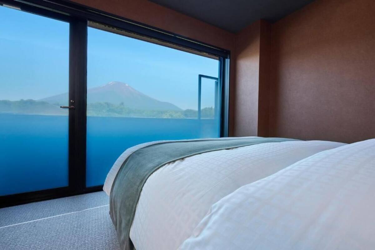 Un dormitorio con una cama grande, una puerta corrediza de vidrio que da a un lago con una montaña al fondo.