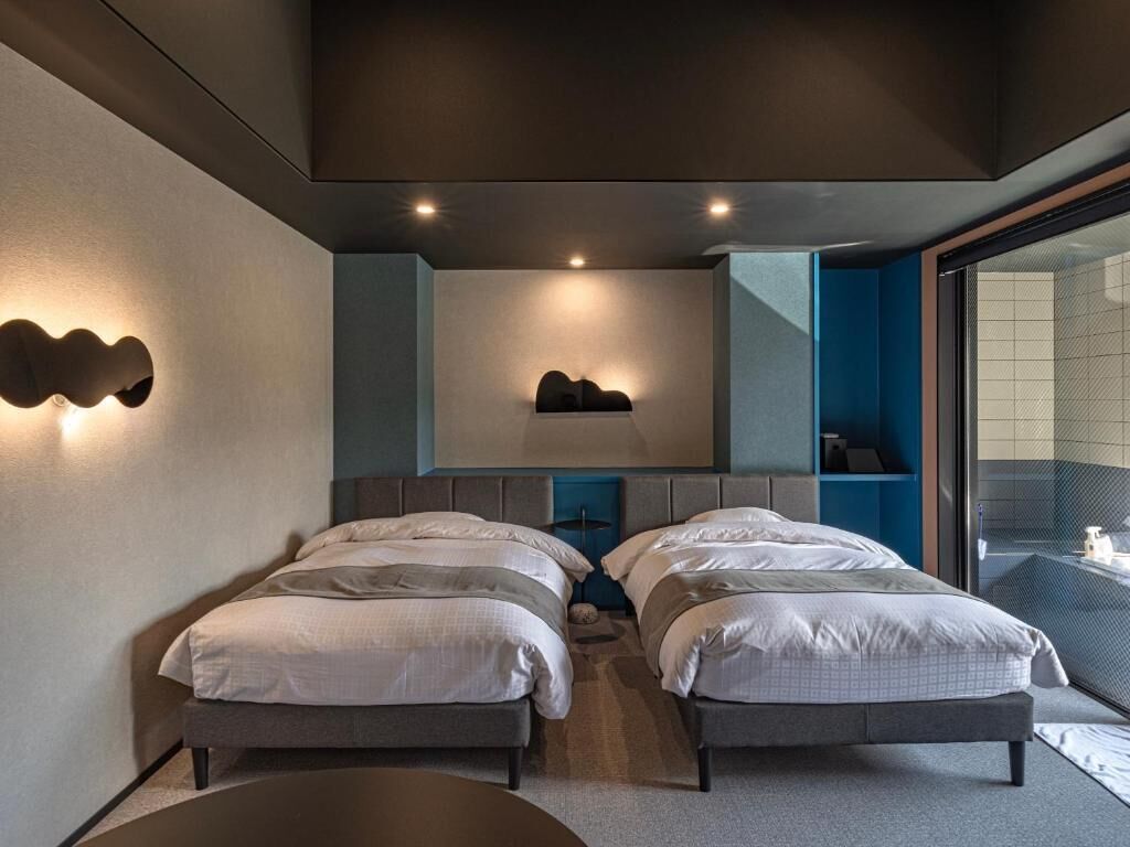 A modern hotel room with two beds, a large window, and a built-in shelf.