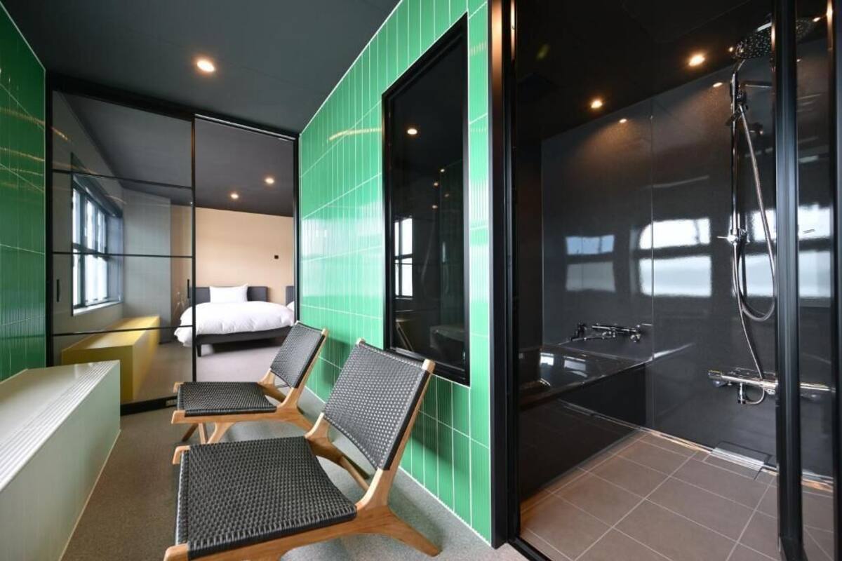Una habitación de hotel moderna con una cama grande, una zona de estar con sillones y un área de ducha separada.