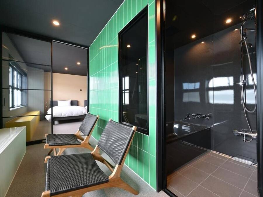 A modern hotel room with a large bed, a sitting area with chairs, and a separate shower area.