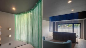 Une chambre moderne avec un lit aux lignes courbes, un canapé bleu et une grande fenêtre donnant sur l’extérieur.