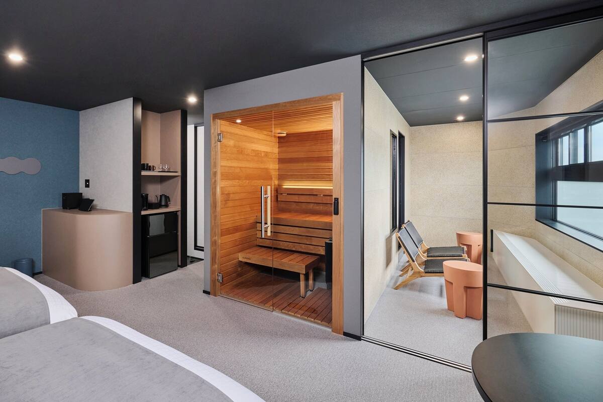 Una habitación de hotel moderna con cama, escritorio, zona de estar y sauna.