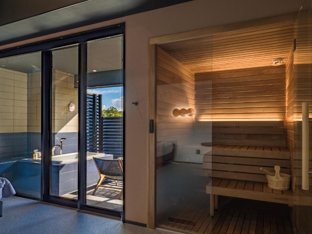 Un bany modern amb una porta de vidre que dona a la zona de dutxa, sauna de fusta i vista exterior.