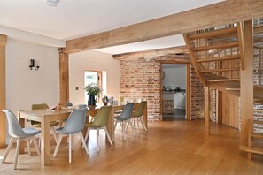A dining area with a wooden table and chairs, a brick wall, and a staircase. - Hare Farm Oast - amazing views - ideal for family celebrations (Rye)