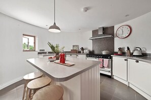 A modern kitchen with a central island, white cabinetry, a stove, and a clock on the wall. - Hare Farm Oast - amazing views - ideal for family celebrations (Rye)