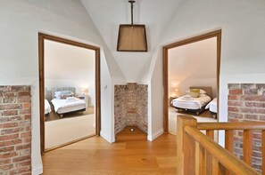 A hallway with wooden flooring, brick walls, and two bedrooms with beds and nightstands. - Hare Farm Oast - amazing views - ideal for family celebrations (Rye)