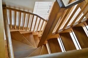 A wooden staircase with a curved design, leading to a room with a sloped ceiling and a window with blinds. - Hare Farm Oast - amazing views - ideal for family celebrations (Rye)