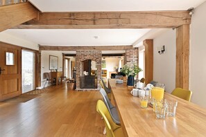 A spacious living area with a wooden floor, a brick fireplace, and a dining table set with glasses and a vase. - Hare Farm Oast - amazing views - ideal for family celebrations (Rye)