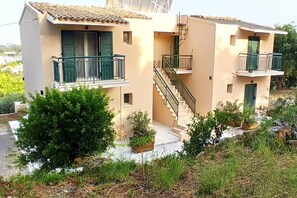 Ein zweistöckiges Gebäude mit Balkonen, einer Treppe und einem kleinen Garten.