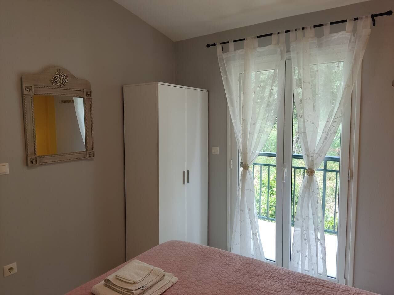 A bedroom with a bed, a wardrobe, a mirror, and a window with curtains.