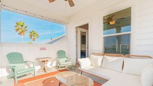 Una habitación soleada con un sofá blanco, dos sillas Adirondack verdes, una mesa de centro de vidrio y vistas a palmeras a través de un amplio ventanal.