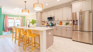 Una cocina moderna con una isla central, electrodomésticos de acero inoxidable y un comedor con sillas amarillas.